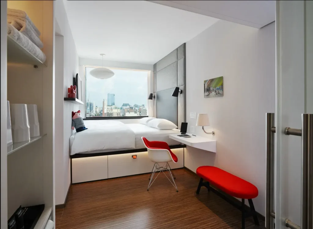 best nyc hotes u nyc under 500, view of standard room at CitizenM Bowery with red accents and white bedding